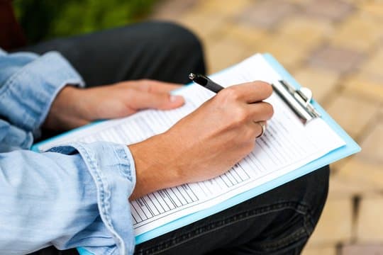 Hands filling out a paper form on a clipboard
